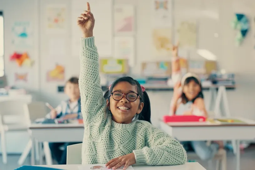 Girl excited with raised hand in classroom for...