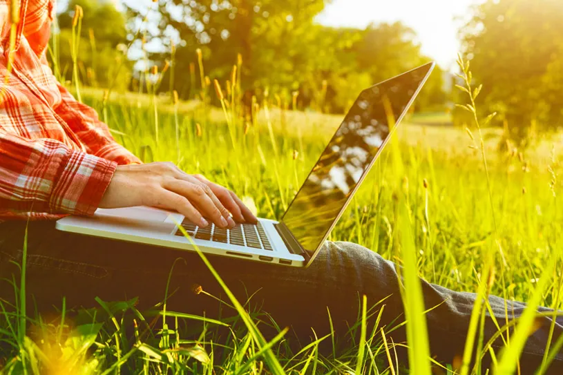 Administrator sitting with laptop in the grass.