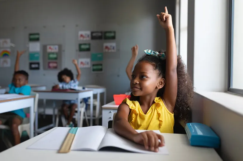 Young girl raising her hand in classroom.