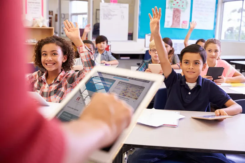 Classroom scene of students at desks using...