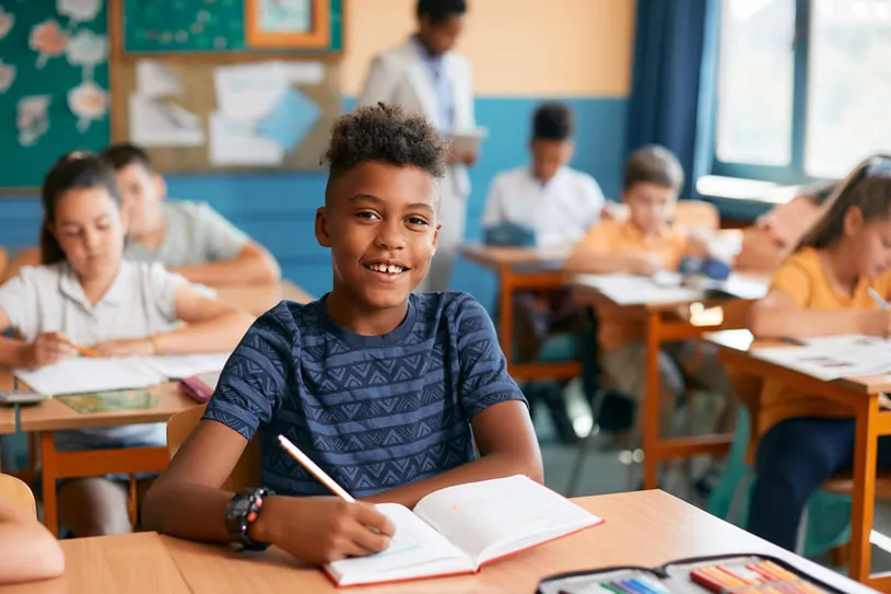 Boy smiling and sitting at a desk in a classroom...