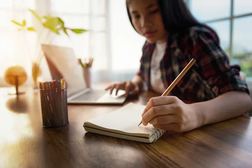 Female student working at a table with pencil,...