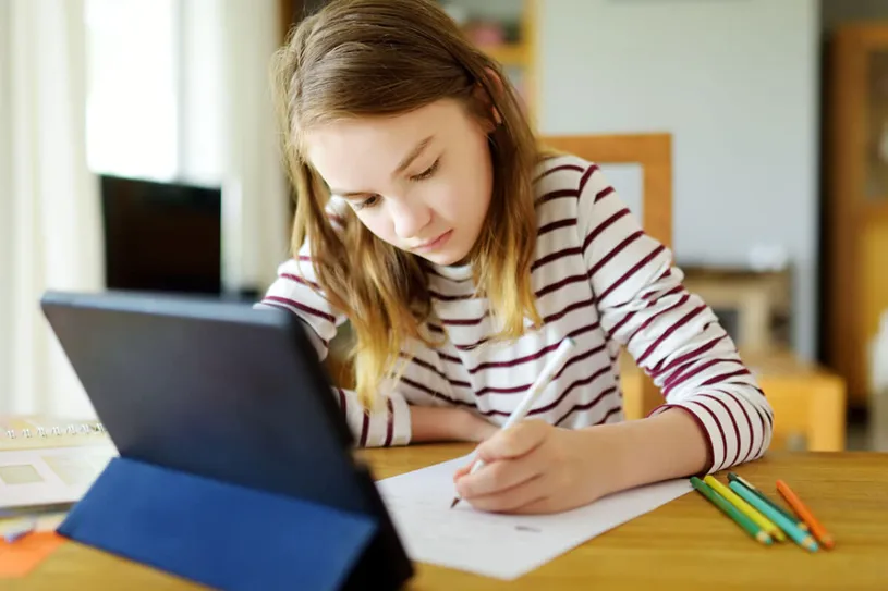 Girl using a device and writing with pencil and...
